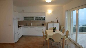 Una cocina moderna con armarios blancos, una mesa de comedor con sillas y un gran ventanal corredera que da a un balcón.