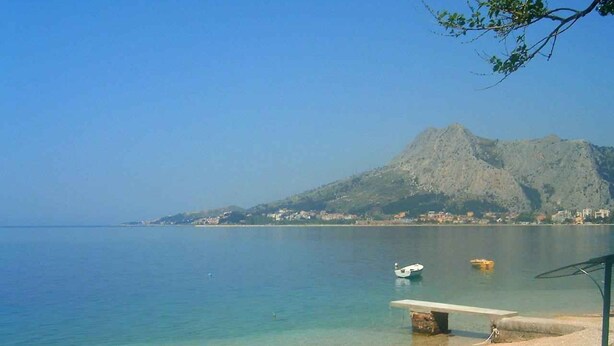 Una playa con agua cristalina, un bote y una montaña al fondo.