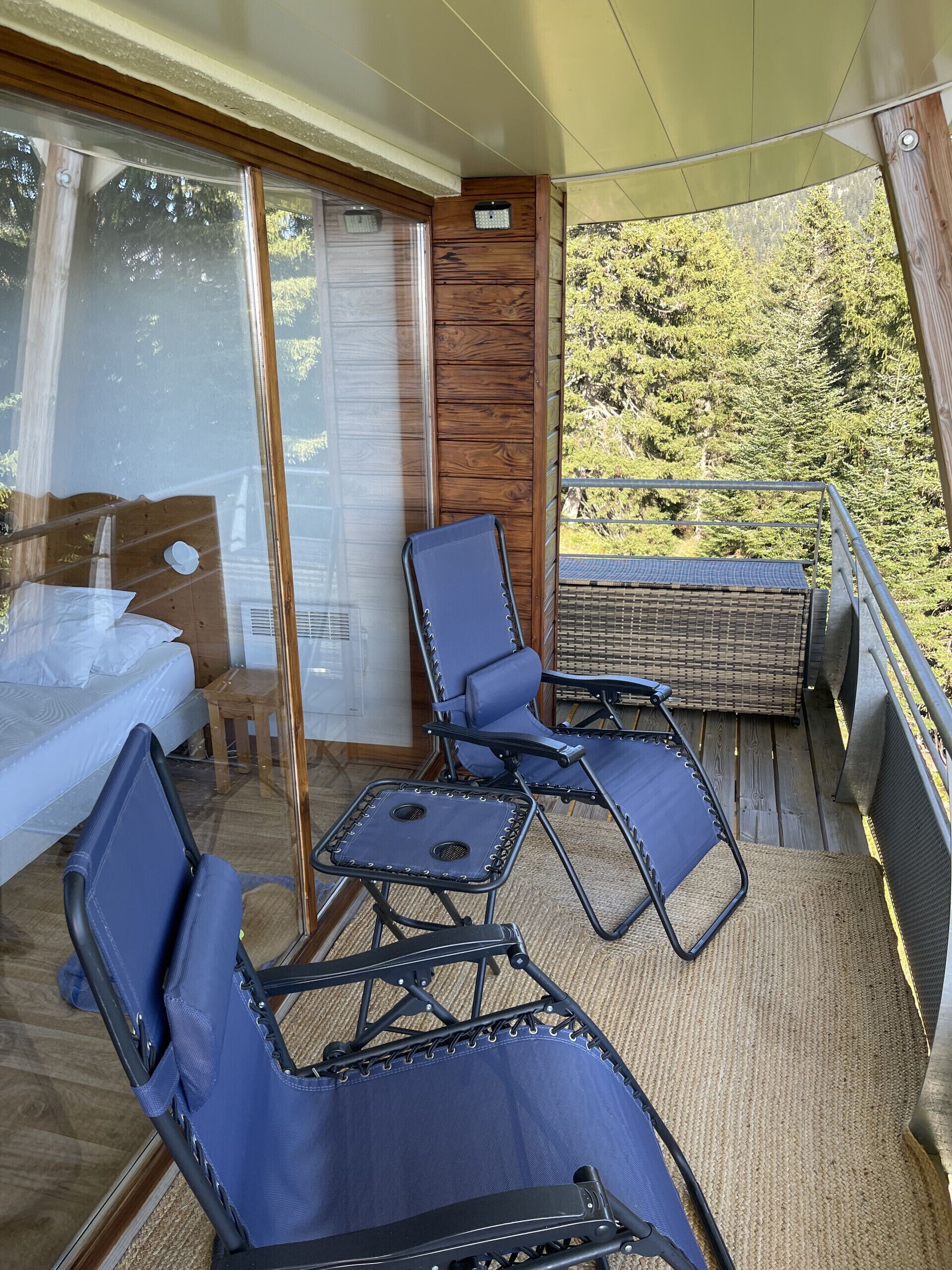 A balcony with two blue lounge chairs, a small table, and a wicker sofa.