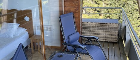 A balcony with two blue lounge chairs, a small table, and a wicker sofa.
