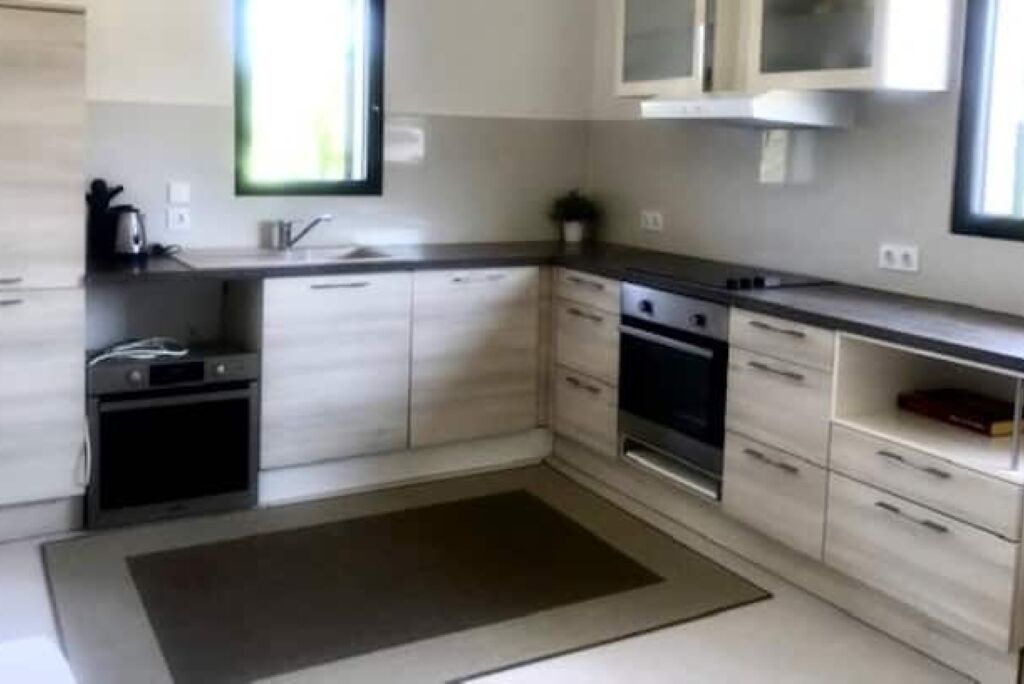 A modern kitchen with light-colored cabinetry, a built-in oven, and a large window providing natural light.