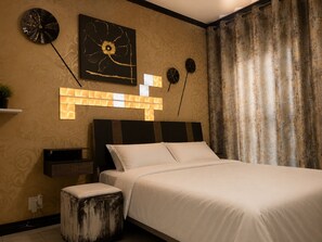 Une chambre d’hôtel comprenant un lit, une table de chevet, une horloge murale, un élément décoratif mural et un rideau.