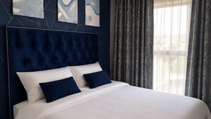 A bed with a tufted headboard, two pillows, and a white bedspread in a room with a geometric-patterned wall and a window with curtains.
