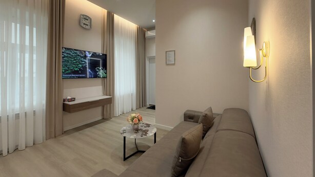 Een moderne woonkamer met een flatscreen televisie, een bank, een bijzettafeltje met bloemen en een wandlamp.