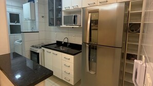 A compact kitchen with white cabinets, a stainless steel refrigerator, a microwave, and a gas stove. - Apartment in Praia Grande with parking, close to the sea (Praia Grande)
