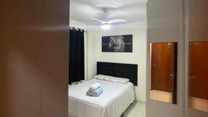 A bedroom with a bed, a ceiling fan, a wall-mounted light, a door, and a window. - Apartment in Praia Grande with parking, close to the sea (Praia Grande)