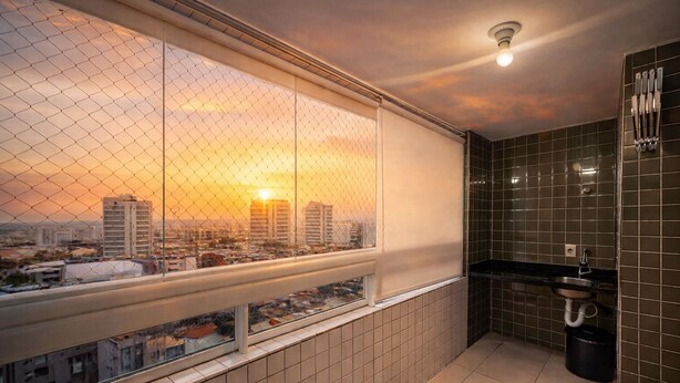 A balcony with a city view at sunset, a small sink, and tiled walls. - Apartment in Praia Grande with parking, close to the sea (Praia Grande)