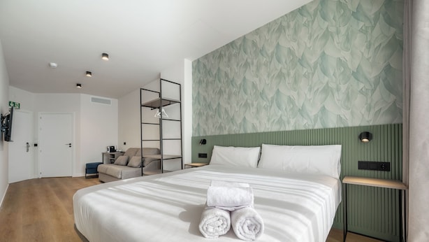 A modern hotel room with a large bed, a green accent wall, and a wooden floor. - Sömn Donostia (San Sebastián)
