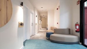 A modern hallway with a curved bench, a fire extinguisher, and a wooden wall feature. - Sömn Donostia (San Sebastián)