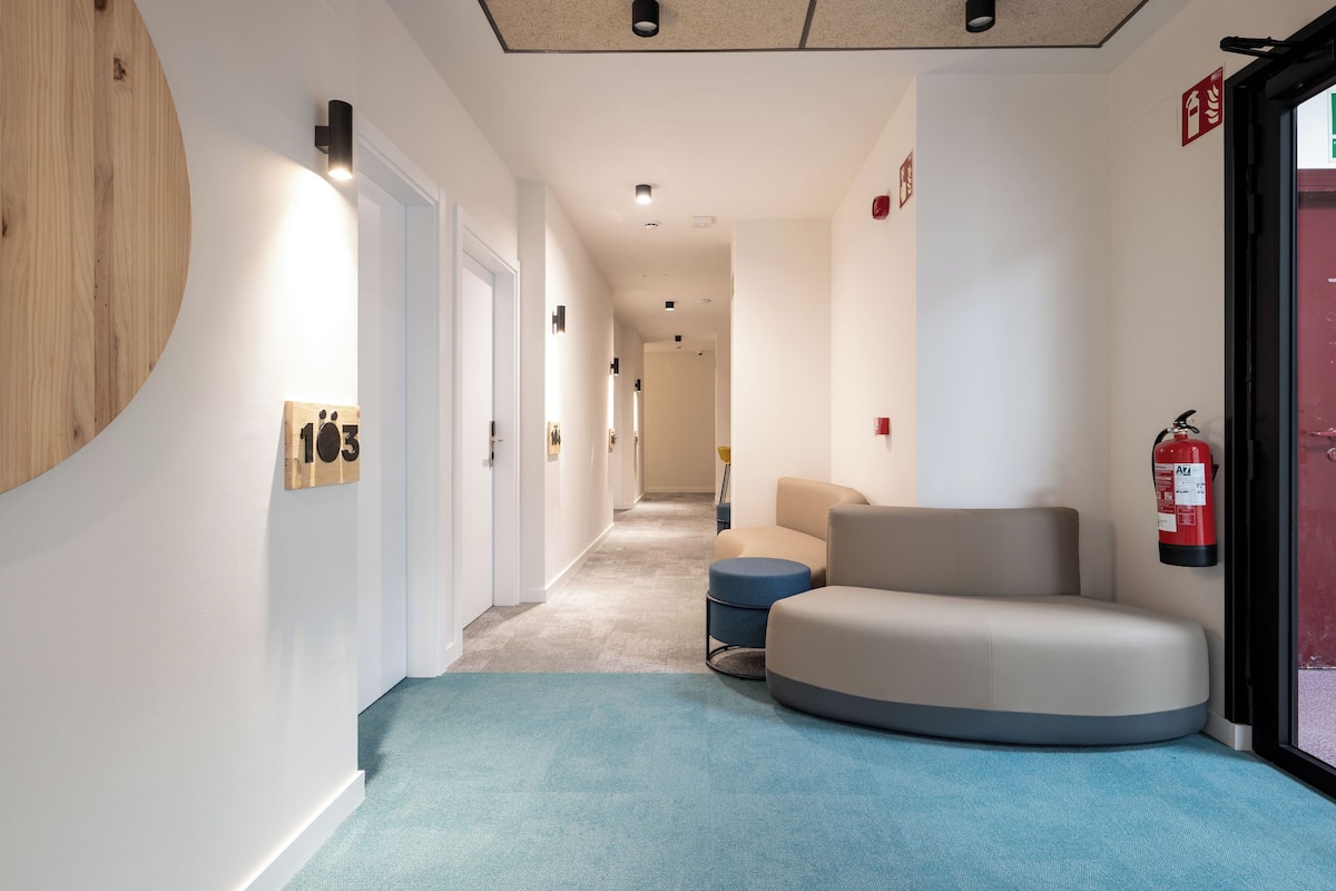 A modern hallway with a curved bench, a fire extinguisher, and a wooden wall feature.
