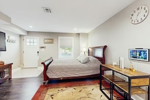 A bedroom with a bed, a desk, a chair, a clock, and a window.
