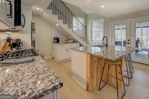 Una cocina con encimera de granito, taburetes de madera, estufa de acero inoxidable y una escalera.