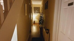 A narrow hallway with wooden flooring, a white door on the right, and a staircase on the left. - Casa Douglas (Lifford)