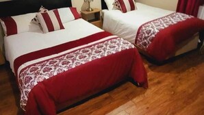A hotel room with two beds, wooden flooring, a painting of flowers on the wall, and a window with curtains. - Casa Douglas (Lifford)