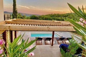 Ein Poolbereich mit Holz-Pergola, Liegestühlen und Blick auf Pool und Grünfläche.