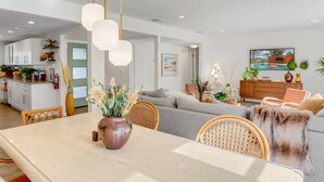 Una sala de estar moderna con comedor, que incluye un sofá, sillas de mimbre, una mesa de madera y un jarrón con flores.