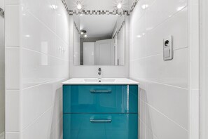 A bathroom with white tiles, a white sink, teal cabinets, and a mirror.