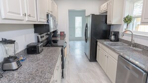 A modern kitchen with white cabinets, granite countertops, a stainless steel refrigerator, and a dishwasher.
