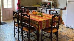 A dining area with a mosaic-tiled floor, wooden chairs, a table with a floral tablecloth, and a hanging light fixture. - Large family home in the country - sleeps 8 (Saint-Seine-sur-Vingeanne)