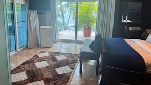 A modern hotel room with a bed, a desk, a chair, a small table, a potted plant, and a view of the outdoors.