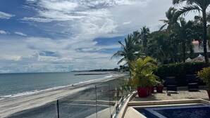 A beach view with a pool area, palm trees, and a clear sky.