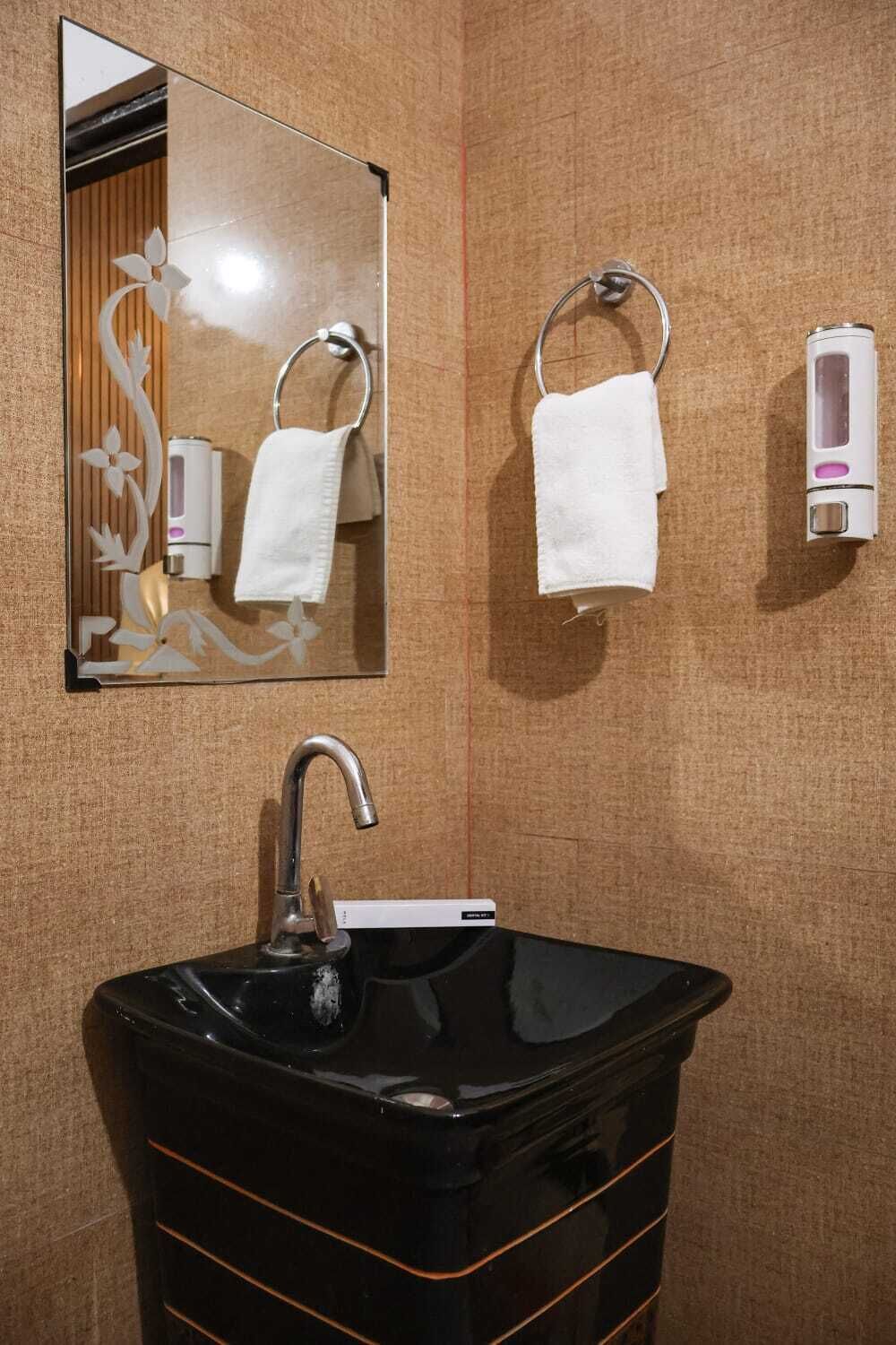 Un baño con un lavamanos negro, un espejo, dos anillas para toallas y un dispensador de jabón.