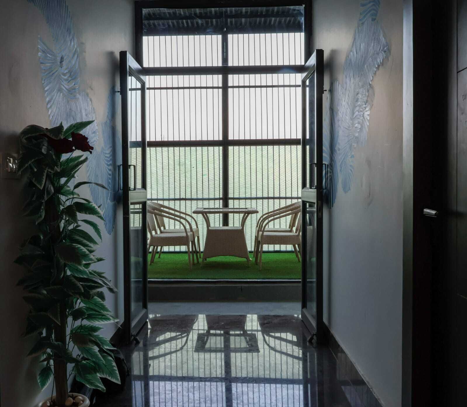 Een open deur die leidt naar een balkon met twee rieten stoelen en een kleine tafel, omgeven door een metalen balustrade.