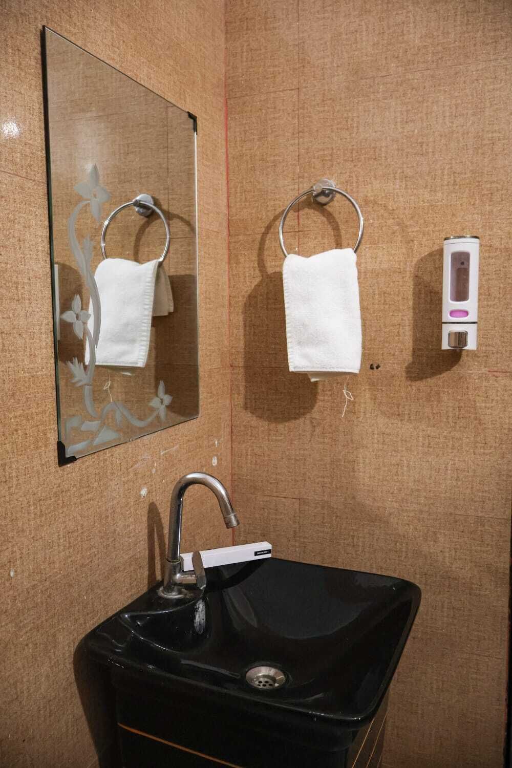Une salle de bain avec un lavabo noir, un miroir, deux porte-serviettes et un distributeur de savon.