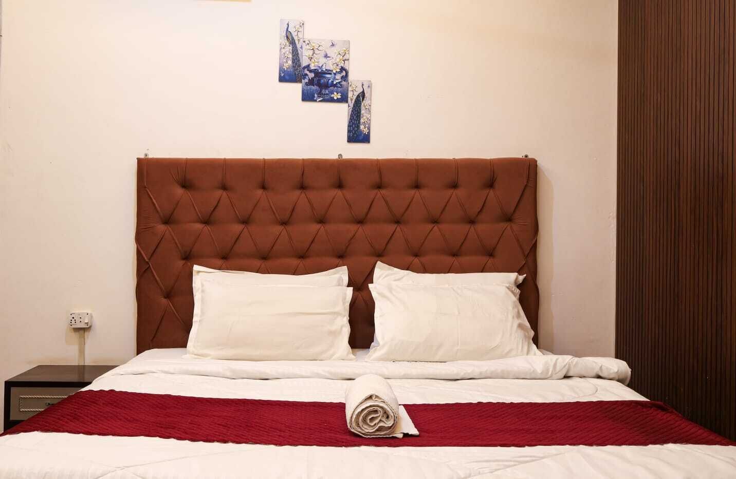 A bed with a tufted headboard, two pillows, a red blanket, and a folded white towel.