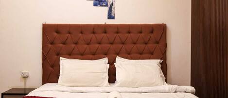 A bed with a tufted headboard, two pillows, a red blanket, and a folded white towel.
