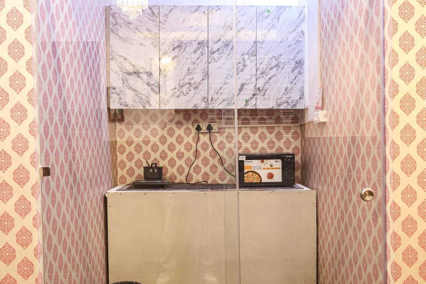 A compact kitchen with patterned wallpaper, a stove, and a box of tea.