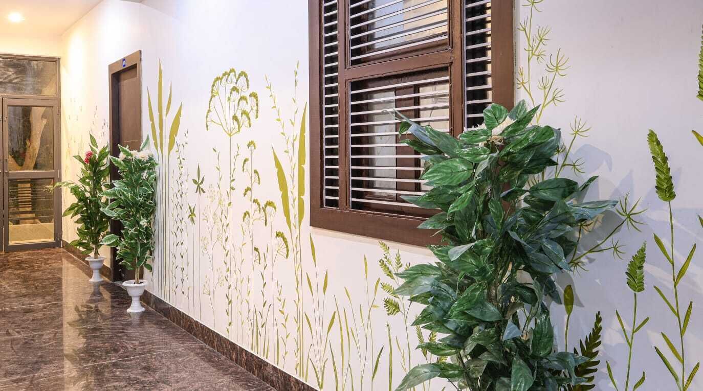 Un couloir doté d’un sol en marbre, de plantes en pot et d’un mur orné d’une fresque représentant des motifs végétaux.