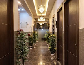 A hallway with potted plants, a chandelier, and a door at the end.