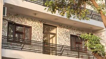 A multi-story building with balconies, a tree in front, and a gated entrance.
