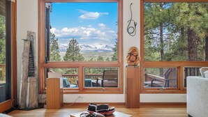 Ein Zimmer mit großen Fenstern und Bergblick, einer Holztreppe und einer gemütlichen Sitzecke mit Teppich und Tisch.
