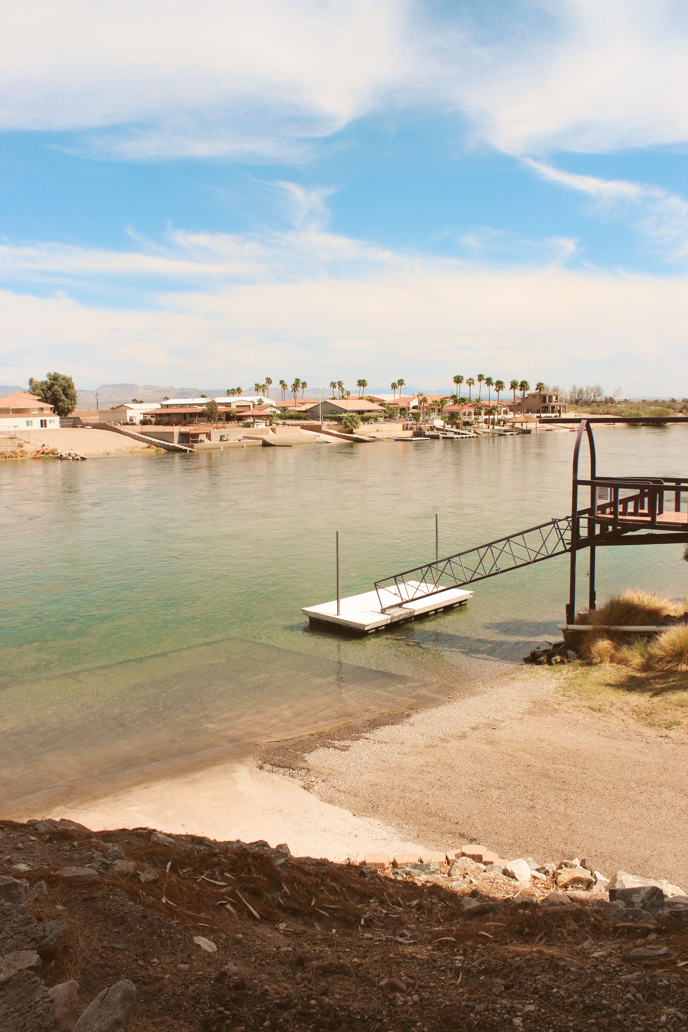 A river with a dock, a sandy shore, and houses in the background.