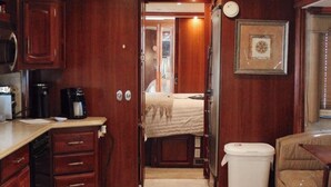 A compact RV interior with a kitchenette, a bed, and a small seating area. - Colorado River RV in Enchanting Needles with beautiful views and boat launch. (Needles)