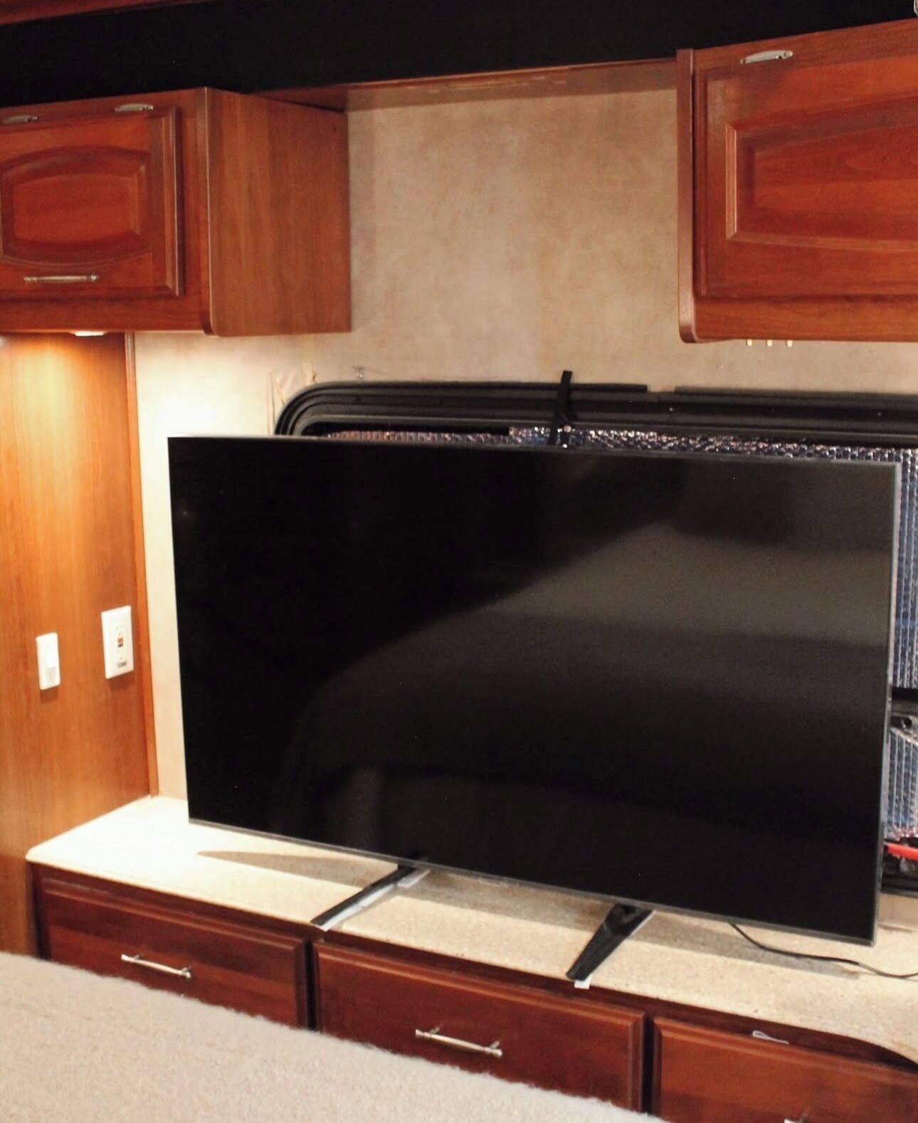 A kitchen with wooden cabinets, a large black flat-screen TV on a white countertop, and a microwave above it.