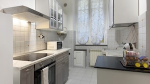 A modern kitchen with white cabinets, a microwave, a small refrigerator, and a window with decorative curtains.