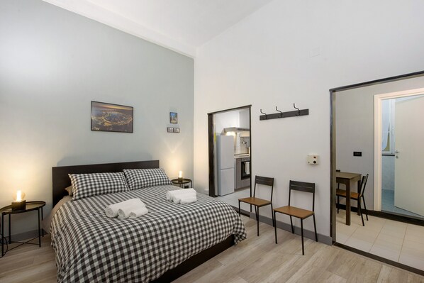 A bedroom with a bed, a nightstand, a chair, a dining table, and a mirror.