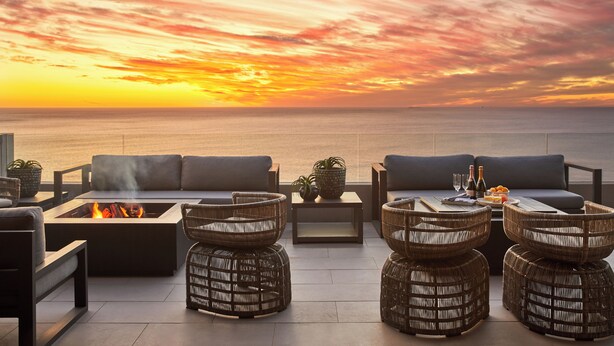 A terrace with a fire pit, wicker furniture, and a view of the sunset over the ocean. - Halcyon Villa (Cape Town)