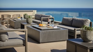 A rooftop terrace with outdoor furniture, a table with drinks, and a view of the ocean. - Halcyon Villa (Cape Town)