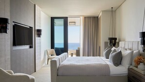 A modern hotel room with a large bed, a TV mounted on the wall, a seating area with a view of the sea, and a balcony. - Halcyon Villa (Cape Town)