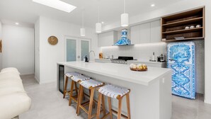 A modern kitchen with white cabinetry, a central island with bar stools, a blue-patterned refrigerator, and pendant lighting.