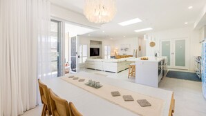 A modern kitchen with a central island, a dining area with a long table, and a living space with a sofa and TV.