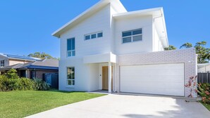 A modern two-story house with a garage, a brick section on the right, and a well-maintained lawn. - Callala Chill Jervis Bay - Short Walk to Creek (Callala Bay)