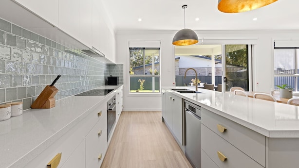 A modern kitchen with a large island, grey tiled backsplash, and a view of the backyard through a sliding door. - Callala Chill Jervis Bay - Short Walk to Creek (Callala Bay)