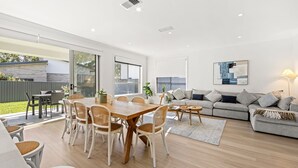 A spacious living area with a dining table, chairs, a sofa, and a coffee table. There is a sliding glass door leading to a patio with outdoor furniture. - Callala Chill Jervis Bay - Short Walk to Creek (Callala Bay)
