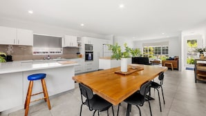 A modern kitchen with white cabinetry, a wooden dining table, and black chairs. - Callala Bay n Beach House - Pet Friendly with Fireplace (Callala Bay)
