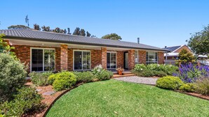 A two-story brick house with large windows, a well-maintained lawn, and a variety of shrubs and plants. - Callala Bay n Beach House - Pet Friendly with Fireplace (Callala Bay)